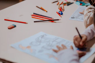 A little girl sitting at a table drawing on a piece of paper
