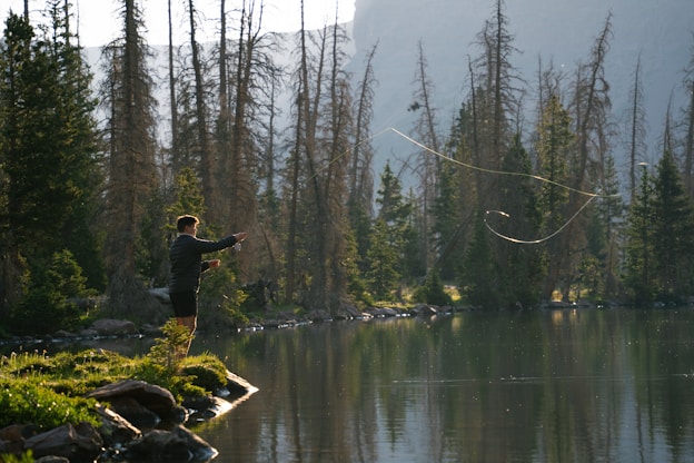 A man standing on top of a lush green field next to a lake