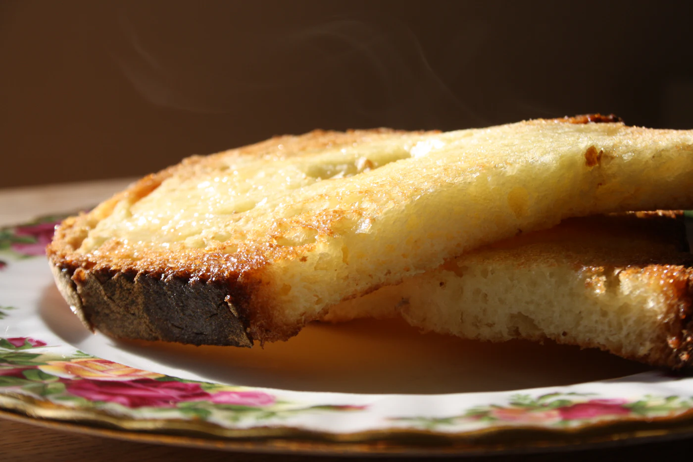 Two slices of hot buttered toast, steam rising, on a floral china plate