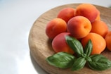 A wooden plate topped with peaches and green leaves