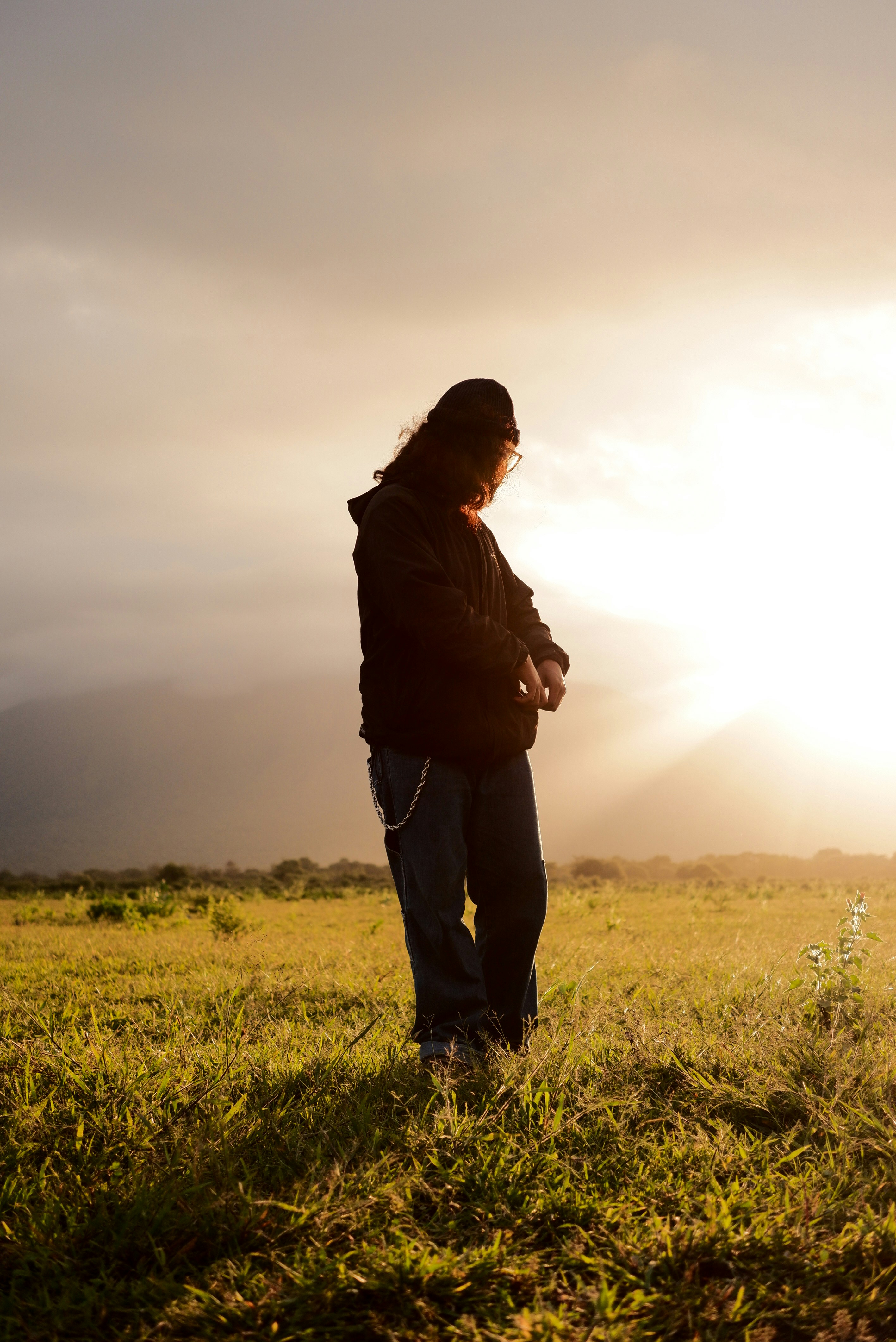 A woman standing in a field with the sun behind her