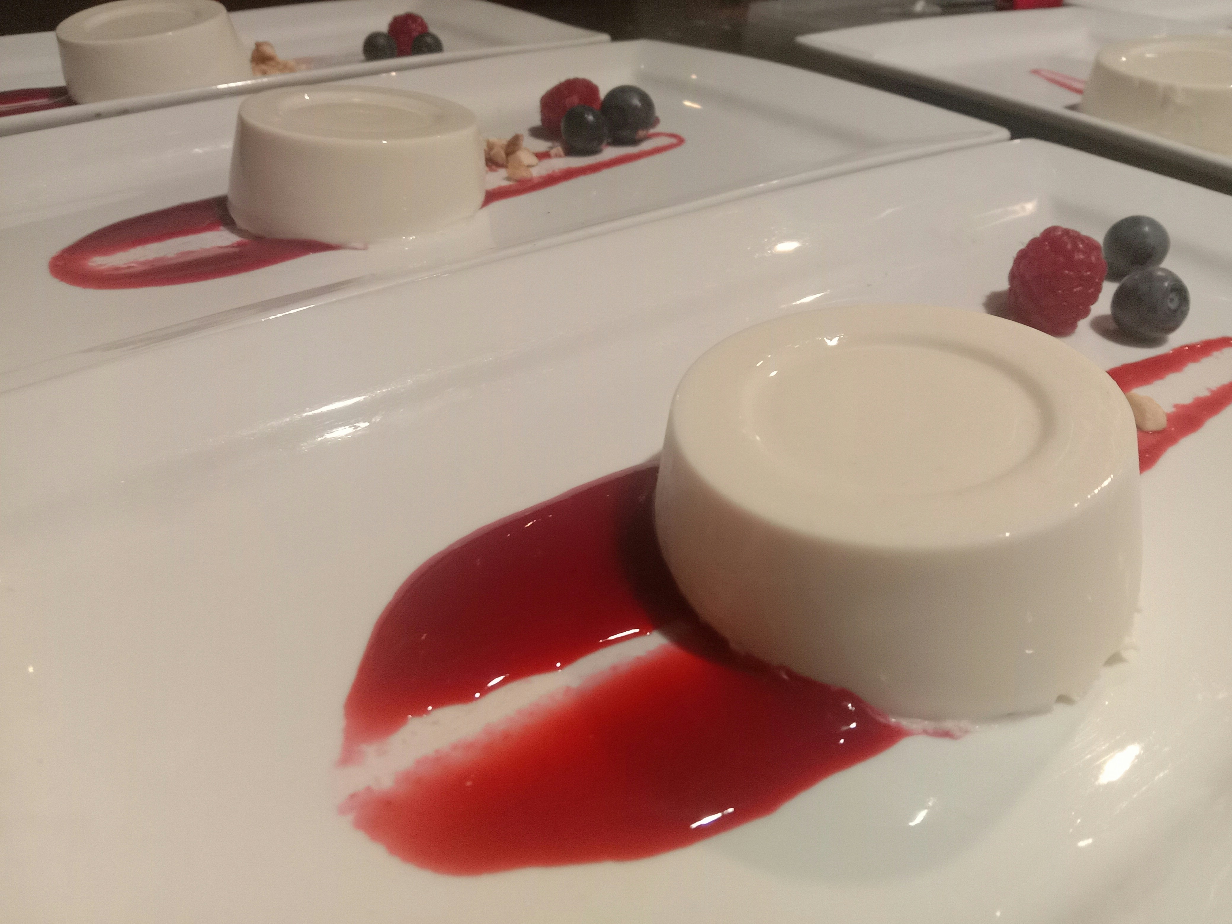 Panna cotta albă cremoasă cu sos roșu de fructe de pădure pe o farfurie elegantă