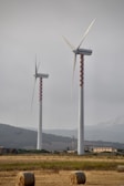 Three windmills in a field with bales of hay
