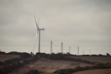 A wind turbine on a hill with power lines in the background