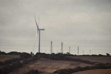 A wind turbine on a hill with power lines in the background