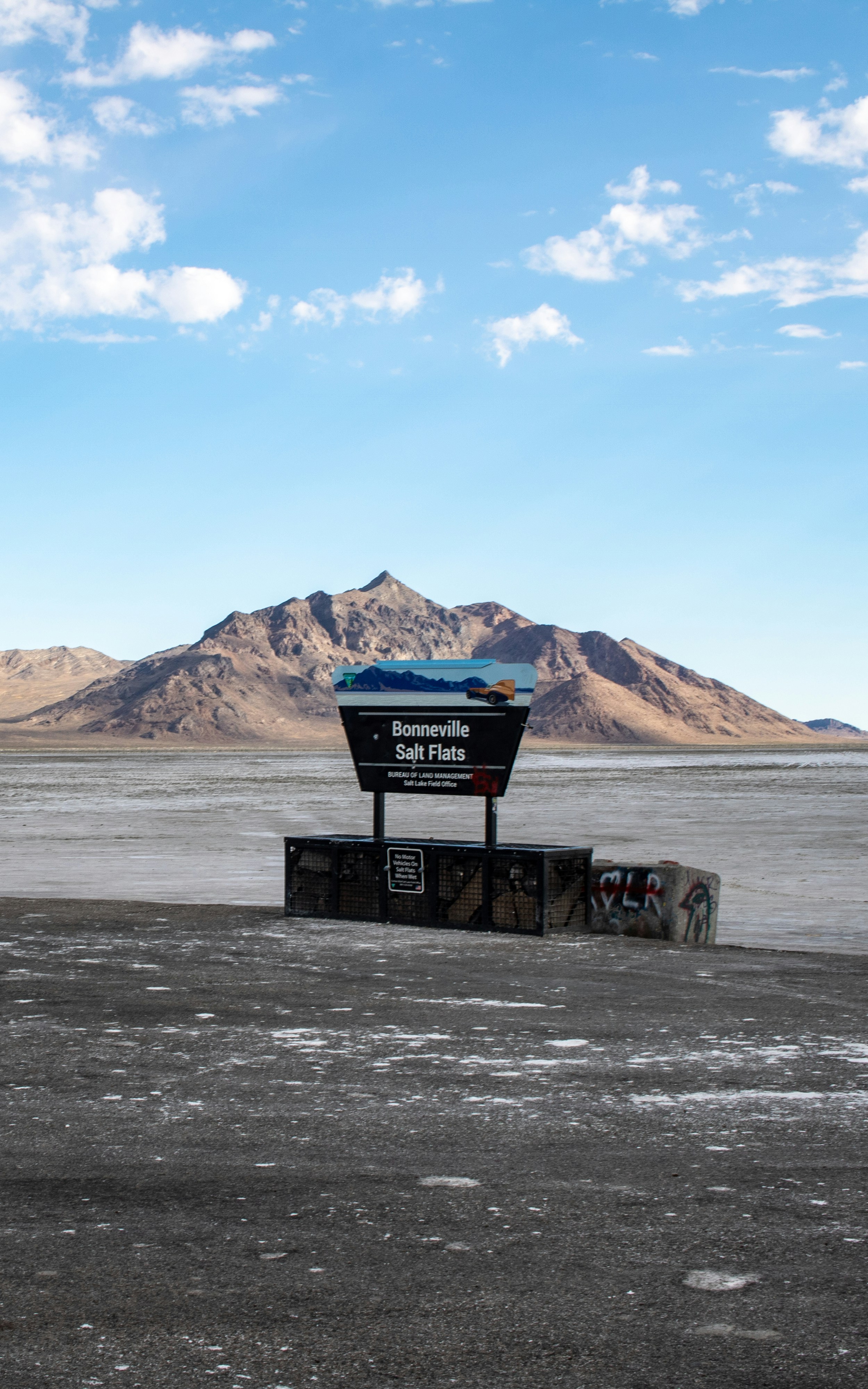 A sign in the middle of a desert with mountains in the background