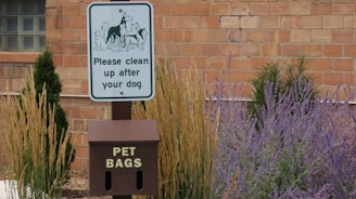 A sign in front of a brick building that says please clean up after your dog