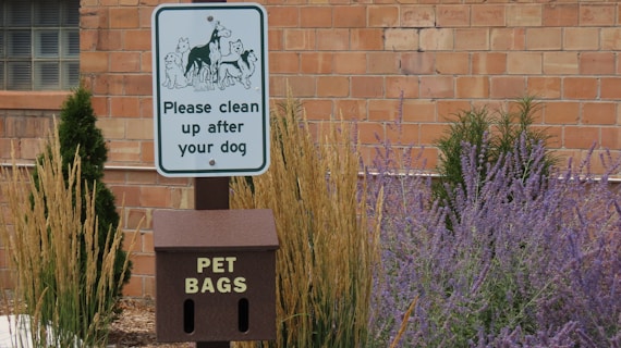 A sign in front of a brick building that says please clean up after your dog