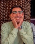 A man wearing glasses sitting at a table with his hands on his face