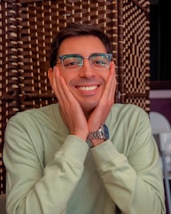 A man wearing glasses sitting at a table with his hands on his face