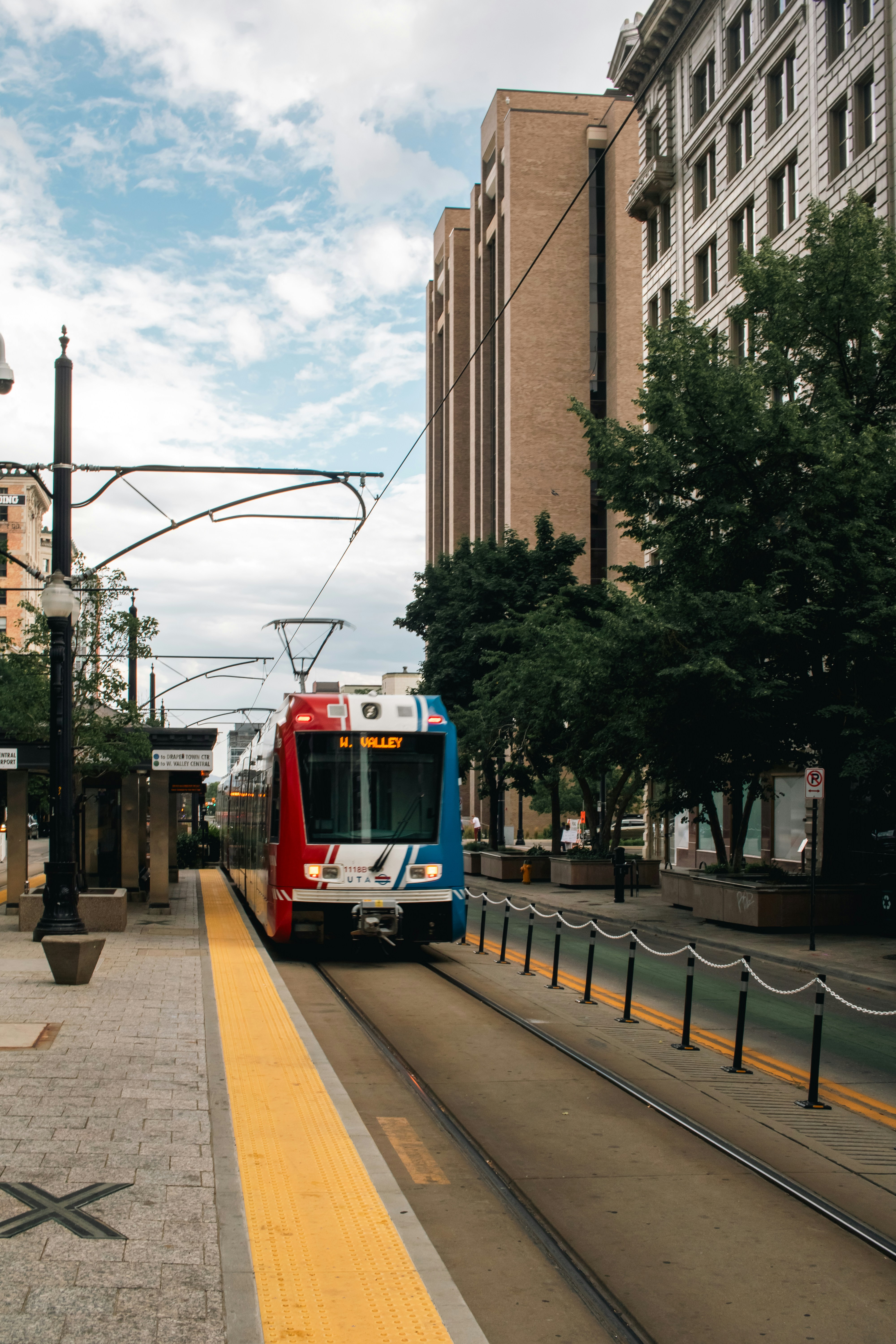 A red and blue train traveling down a street next to tall buildings
