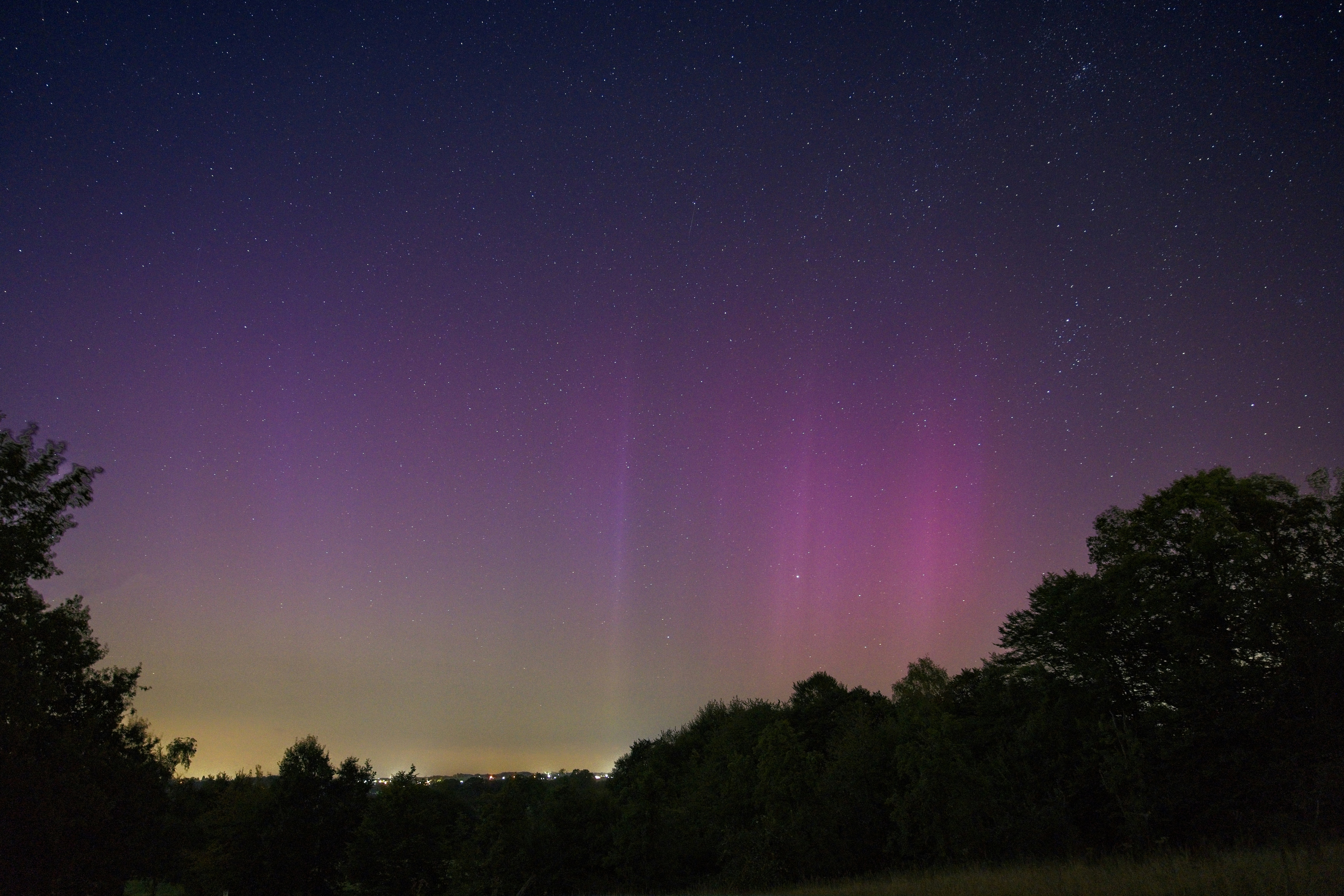 A purple and green light shines in the night sky
