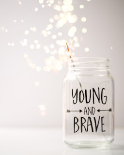 A glass jar with a sparkler in it that says young and brave