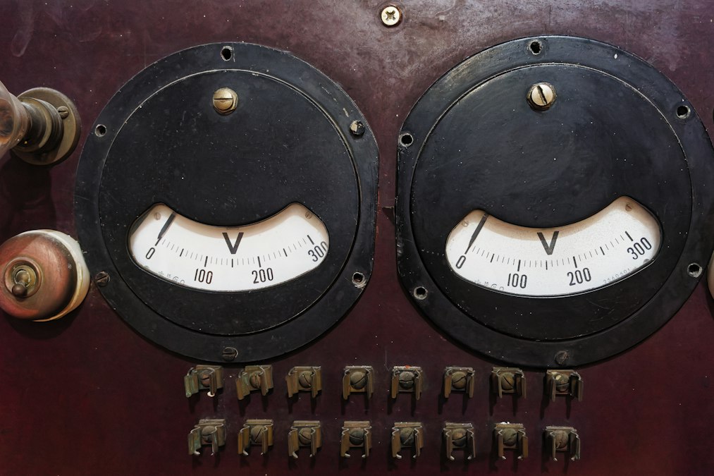 Twee ronde meetinstrumenten en schakelaars op een verweerd houten paneel in een laboratoriumopstelling