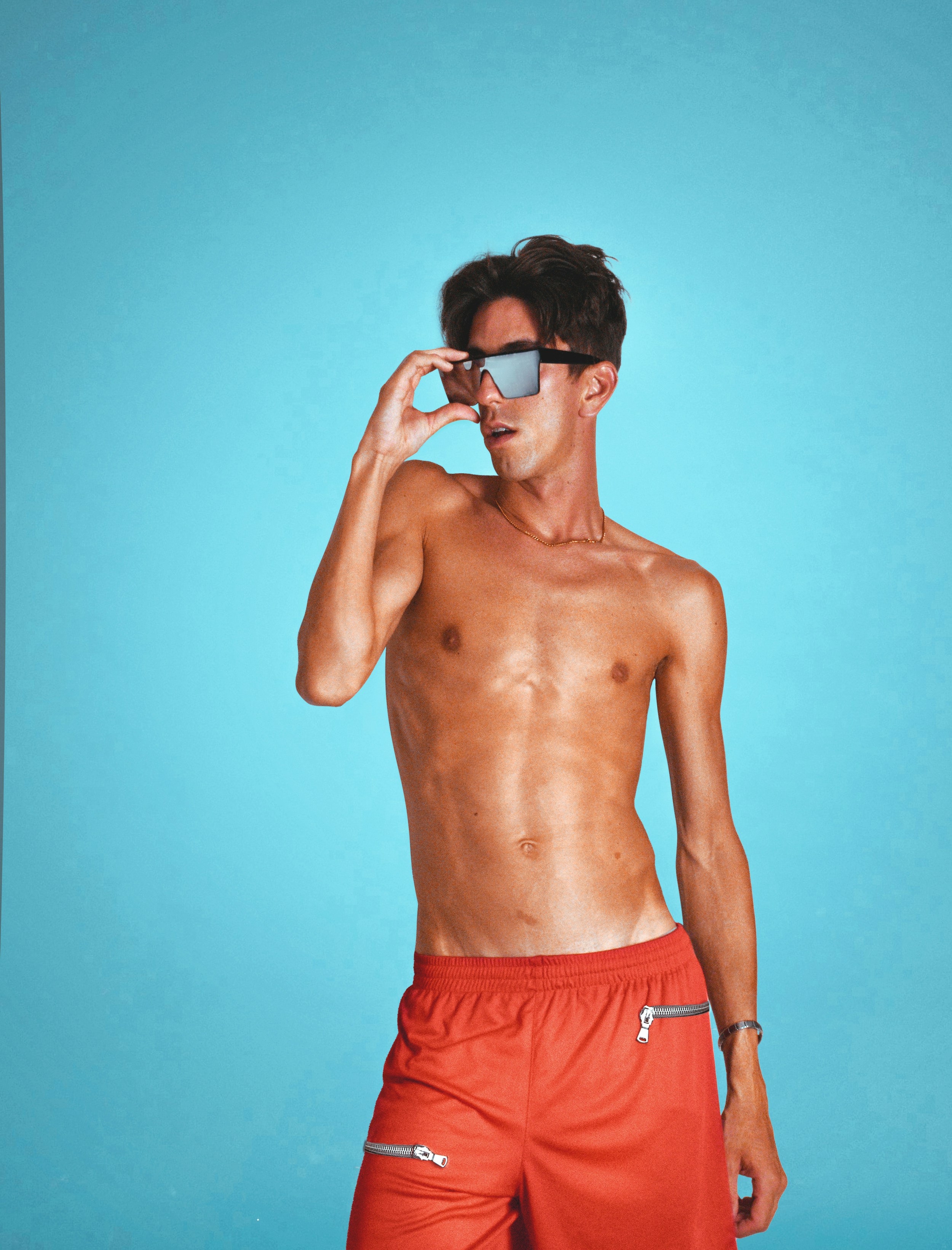 A man with no shirt wearing red swim trunks