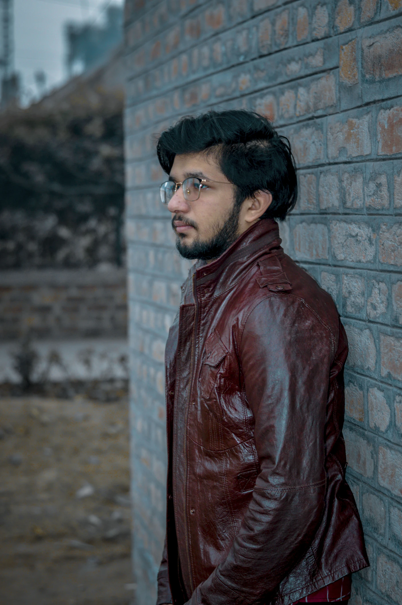 Man in a leather jacket by a brick wall