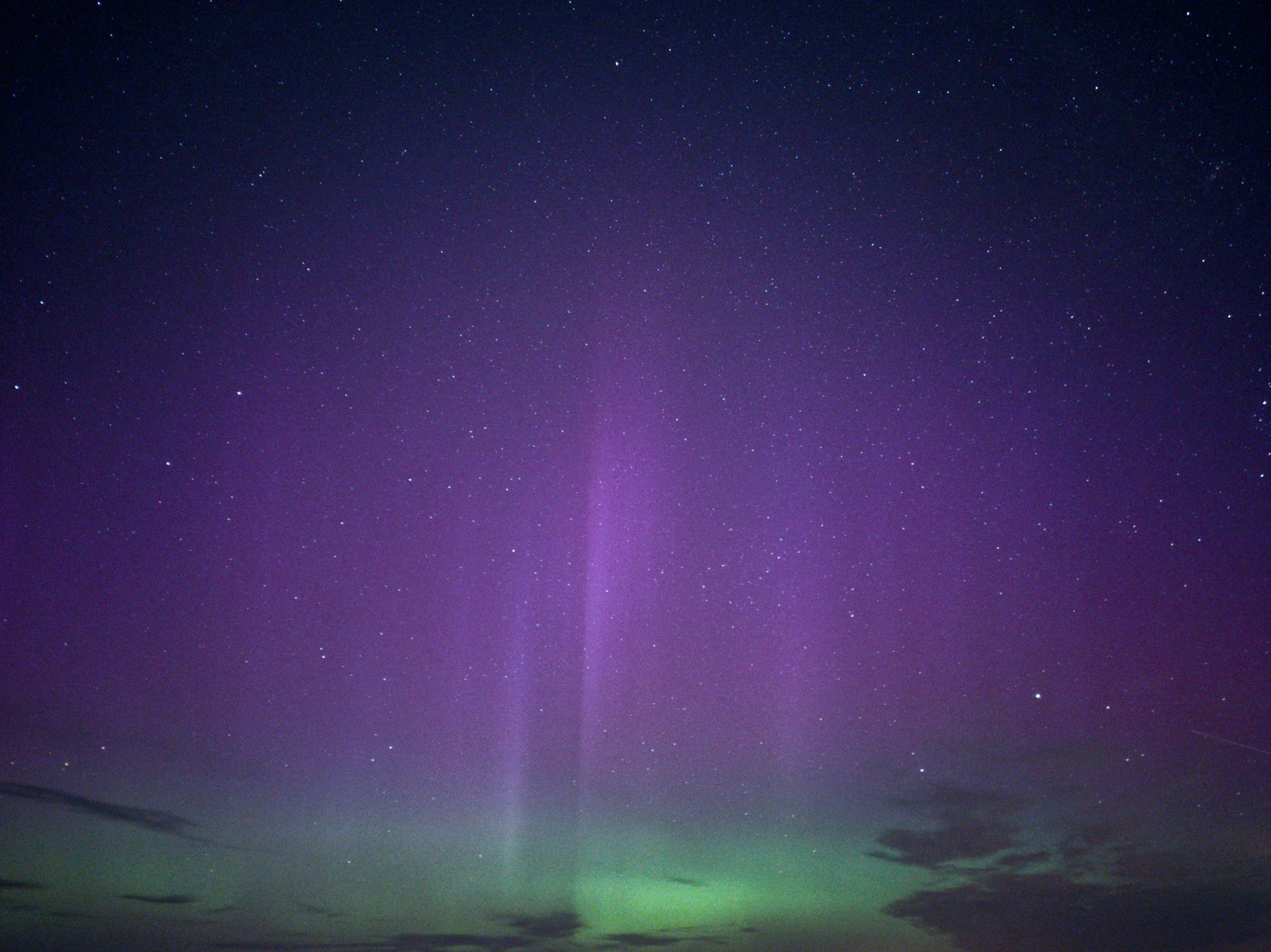A purple and green light shines in the night sky