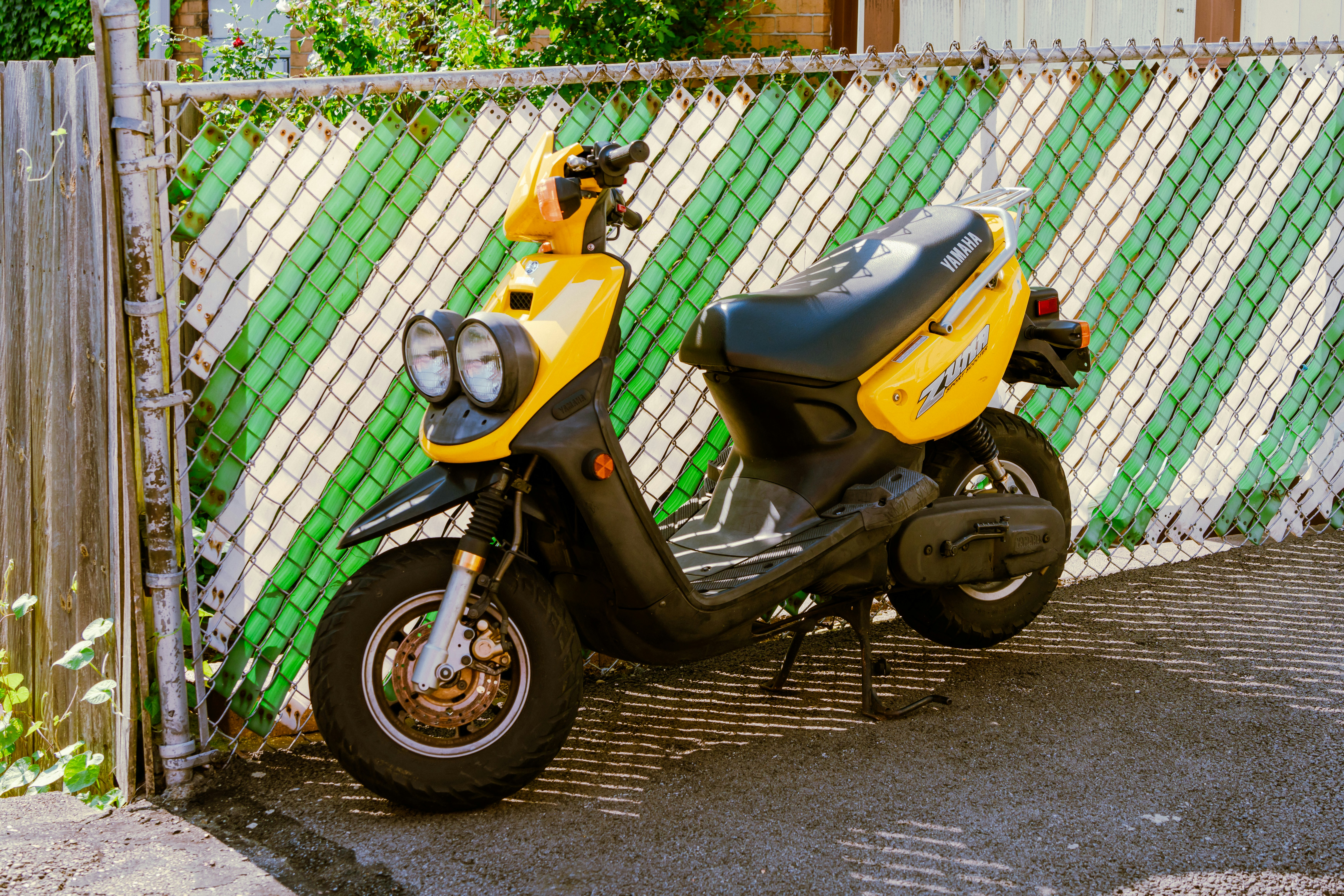 A yellow scooter parked in front of a fence