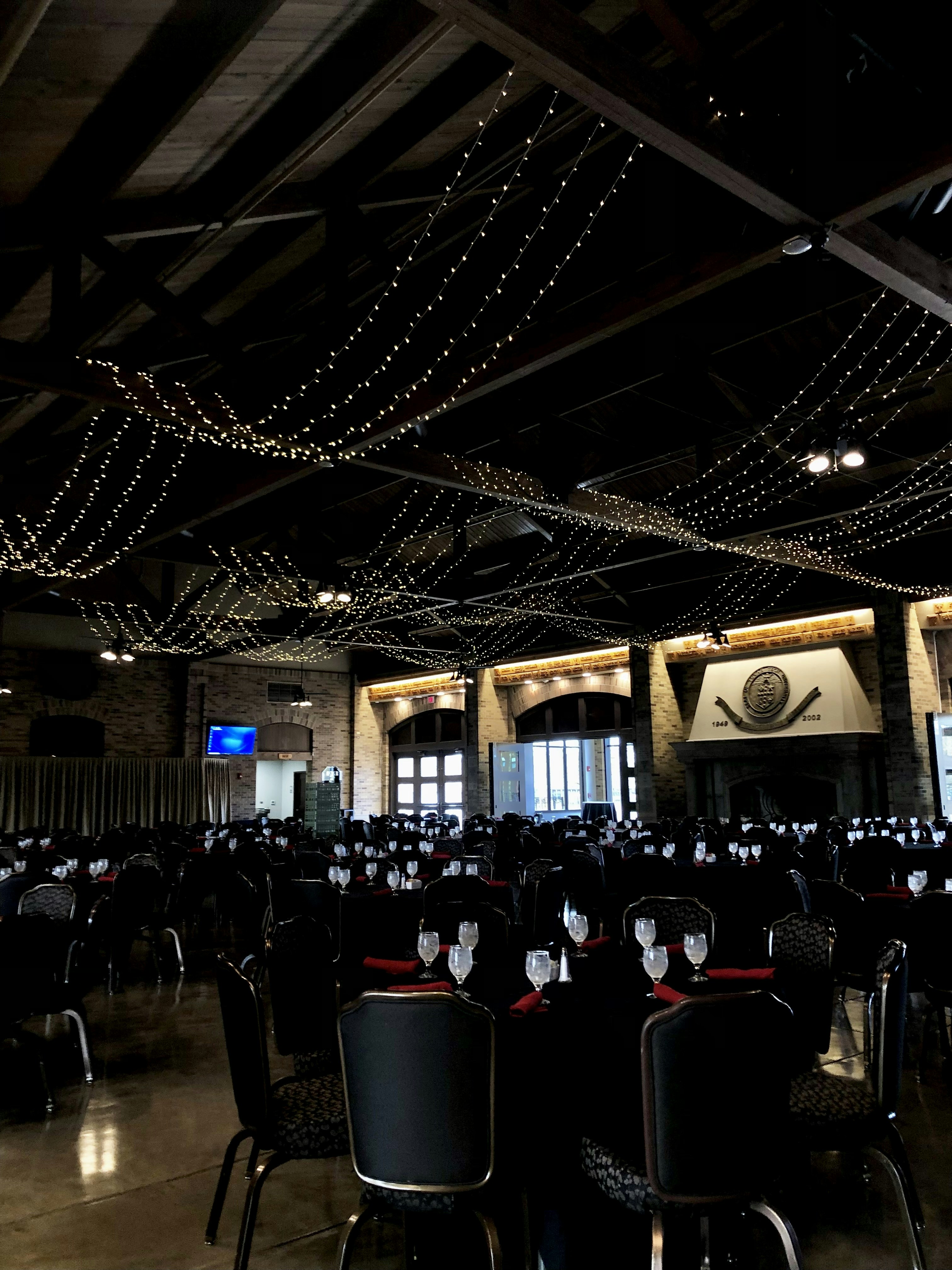 Salle de fête festive avec lumières tamisées chaudes, tables dressées et décoration colorée pour une soirée