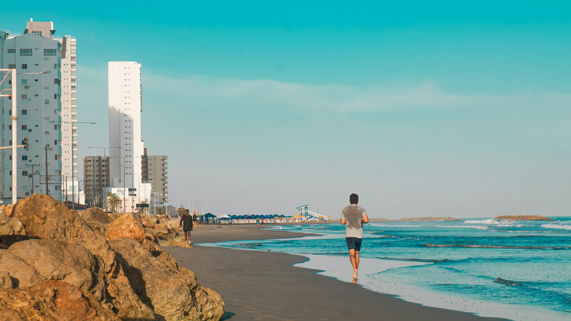 A man walking along a beach next to tall buildings