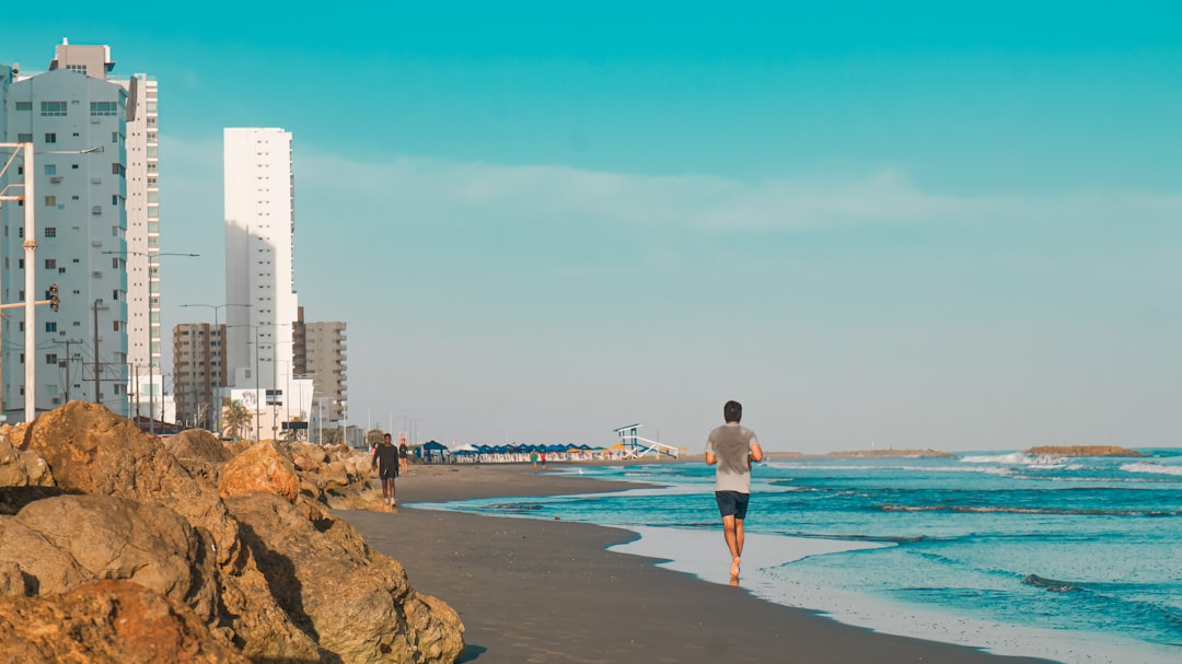 A man walking along a beach next to tall buildings,