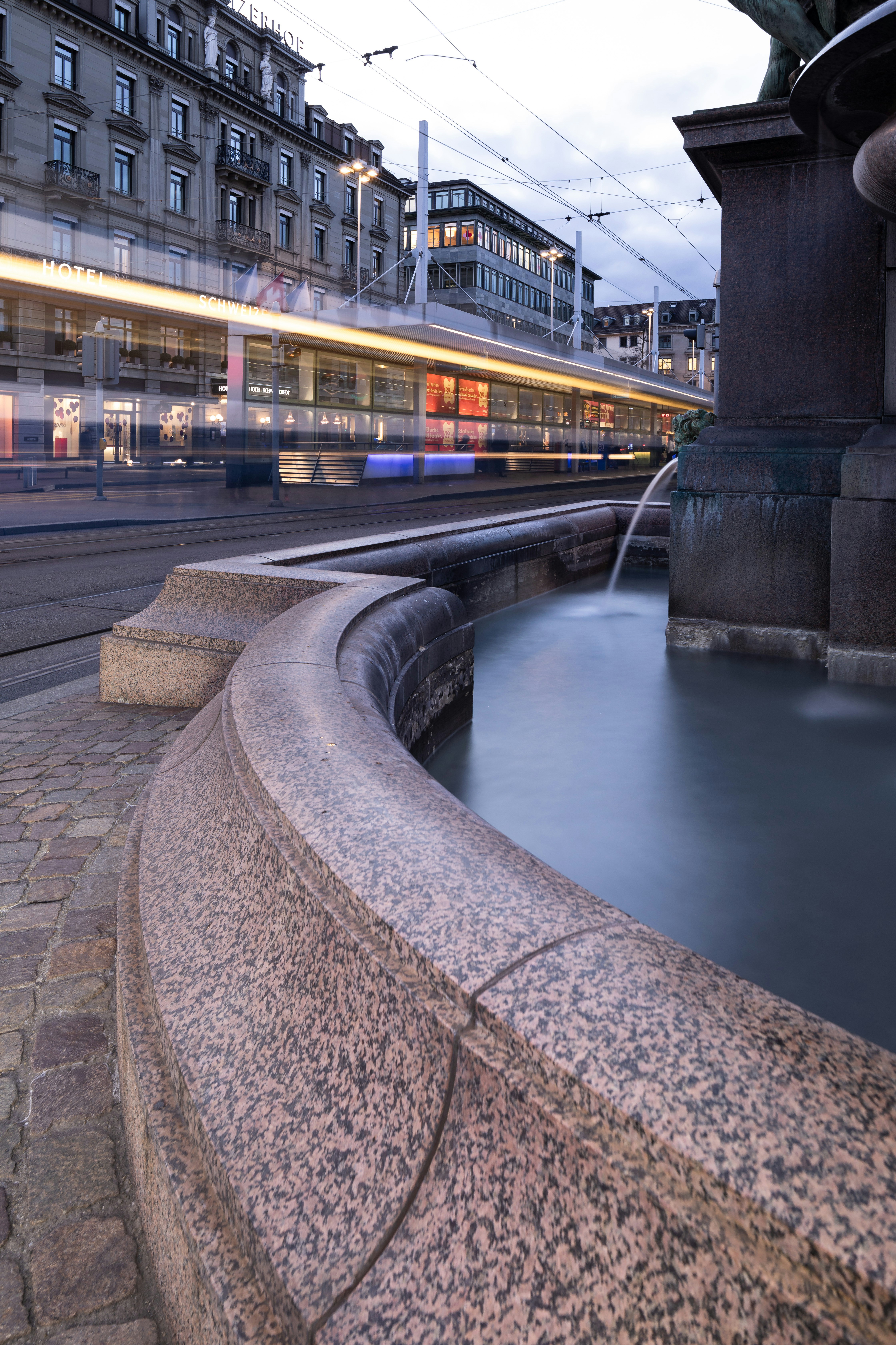 A water fountain with a train passing by in the background
