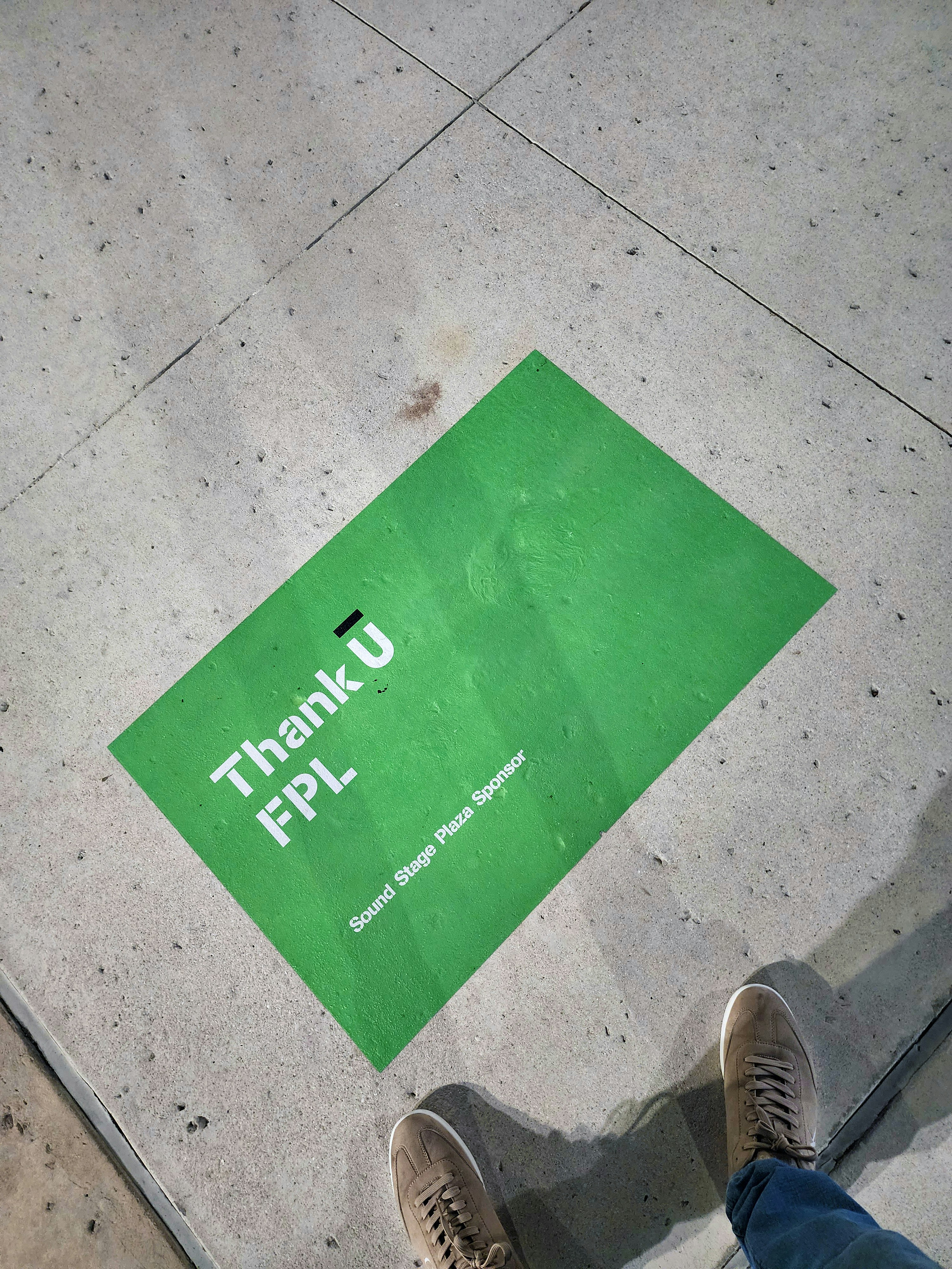 A person standing on a sidewalk next to a green sign