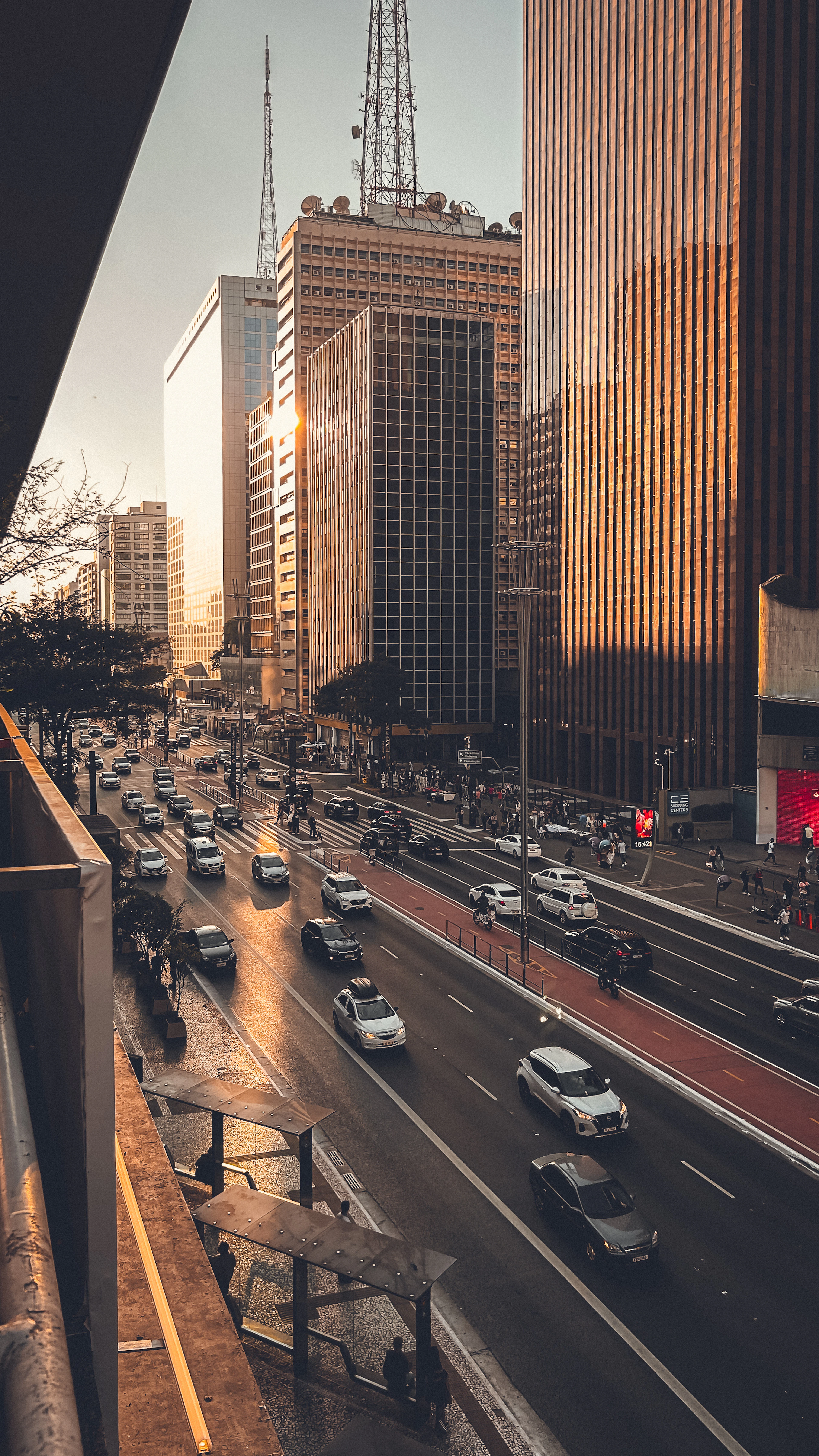 Avenida Paulista at sunset, golden light on high-rises above rush-hour traffic and pedestrians.