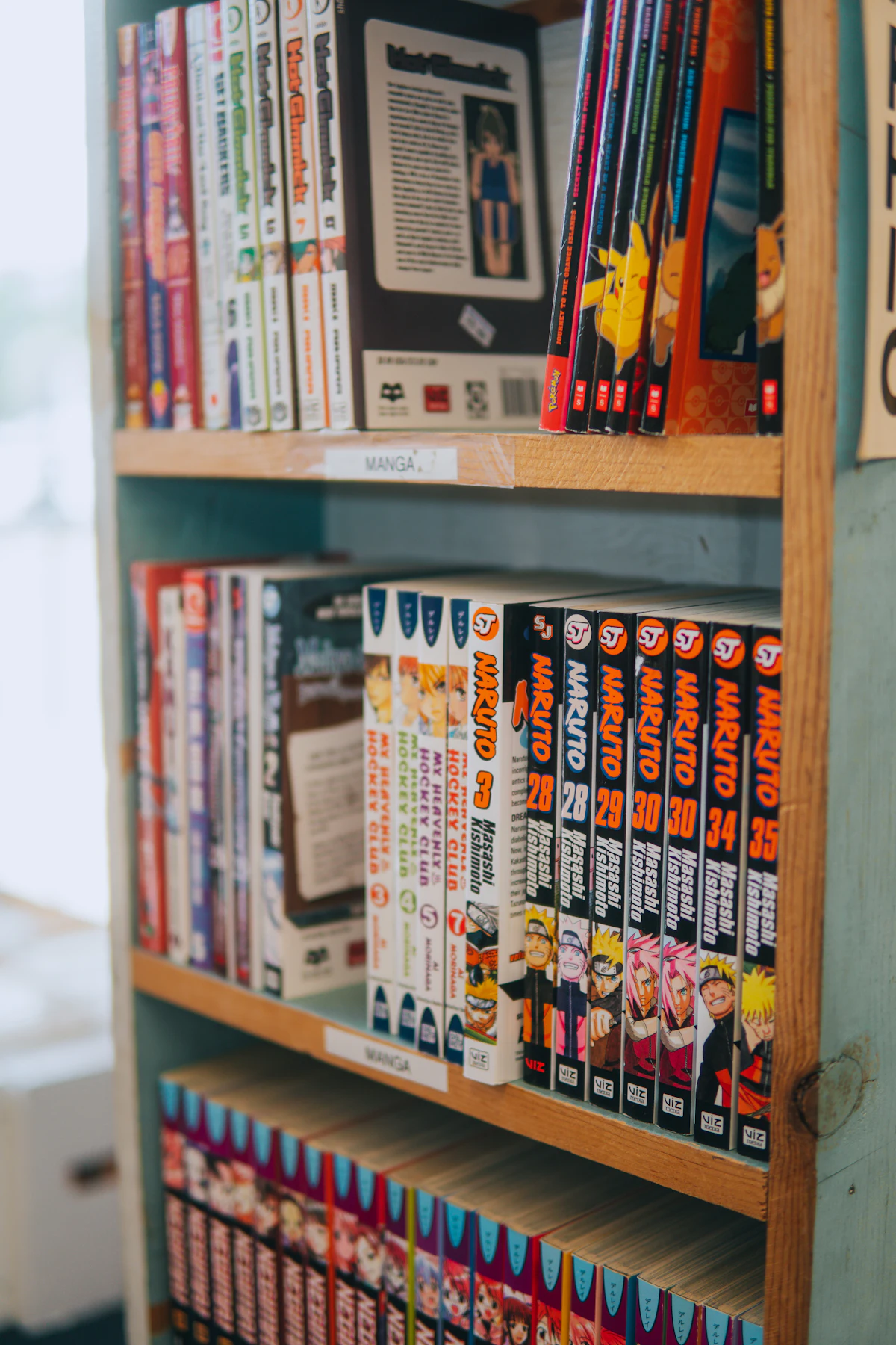 Koleksi manga Naruto berderet rapi di rak buku perpustakaan lengkap dengan label kategori menjadi sumber adaptasi anime populer