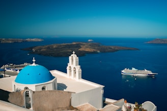 A white church with a blue dome and a cruise ship in the background