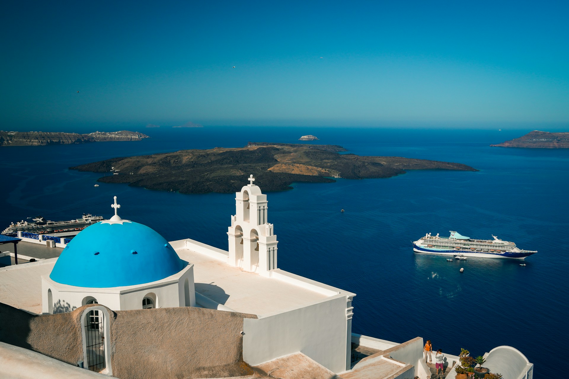 A white church with a blue dome and a cruise ship in the background