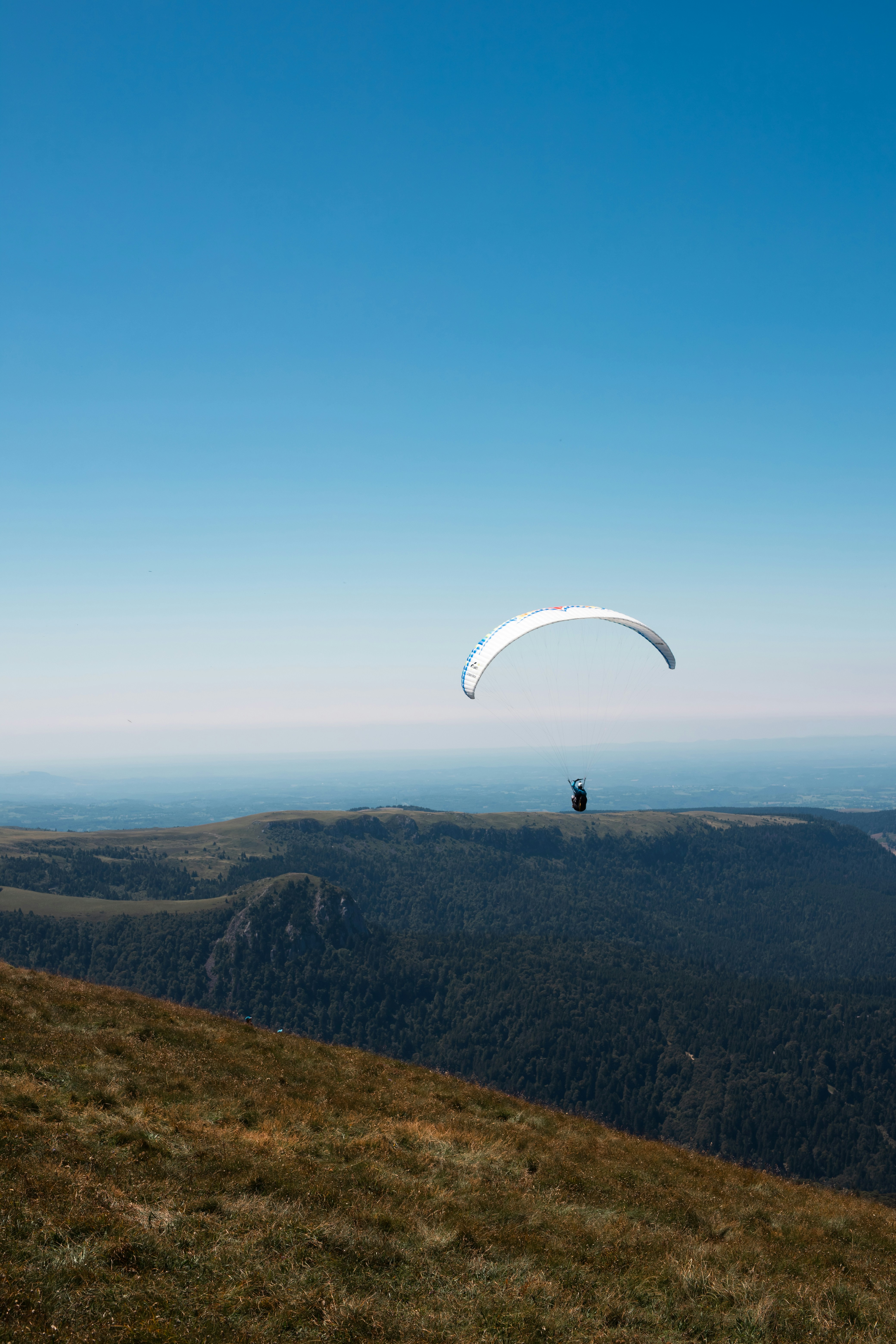 A paraglider is flying over a grassy hill