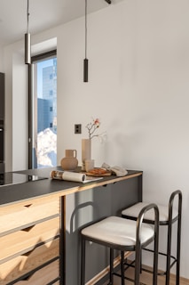 A kitchen with a counter, stools and a window
