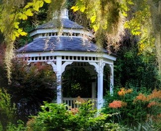 A white gazebo surrounded by trees and flowers