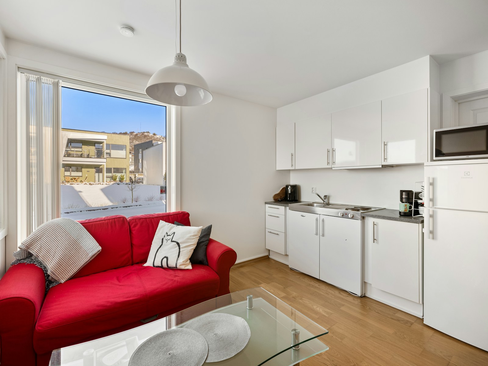 small studio apartment red sofa next to white compact kitchen and window