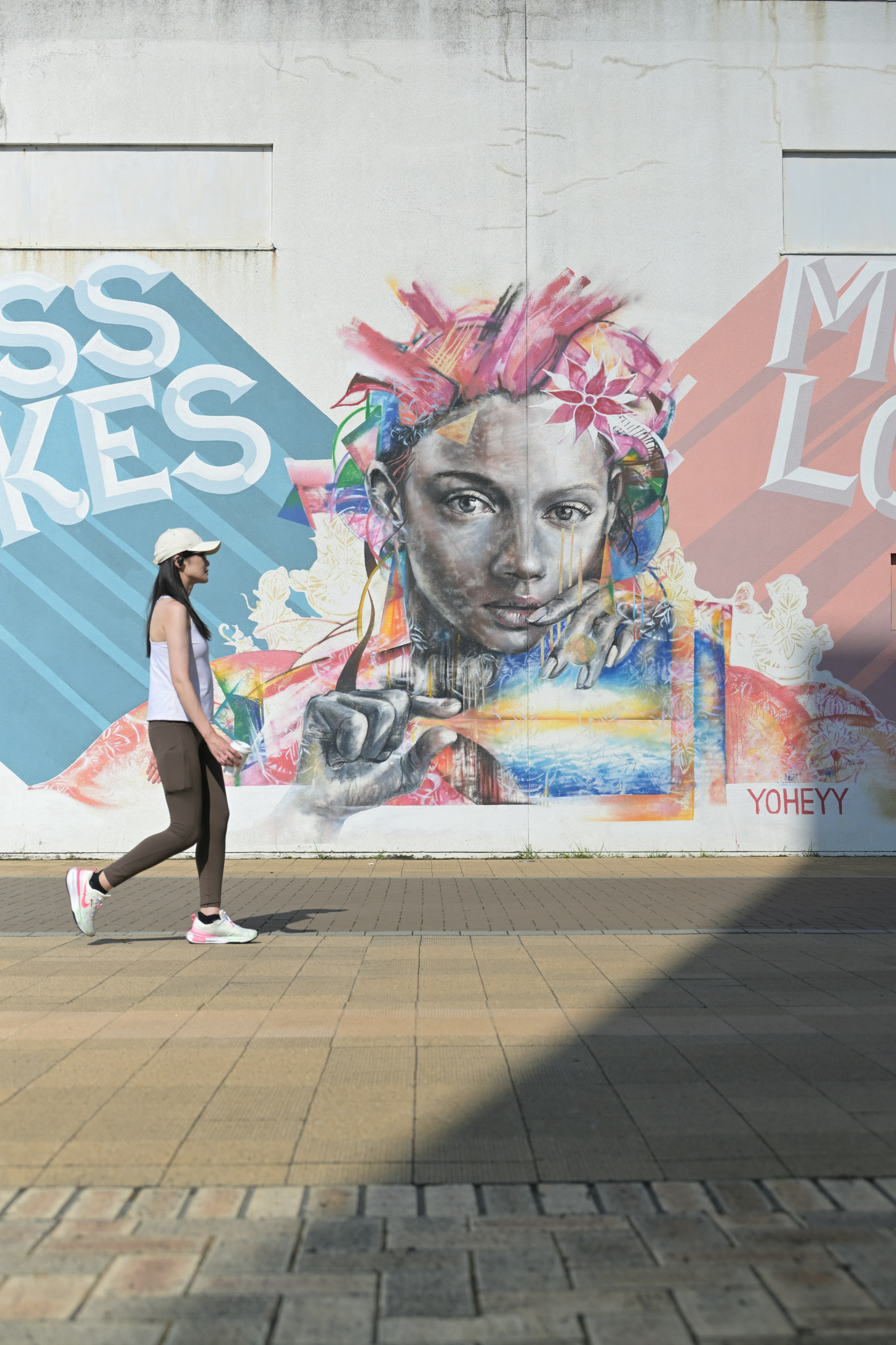 A woman walking down a sidewalk past a wall with a mural on it