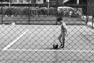A young boy standing on a tennis court holding a ball