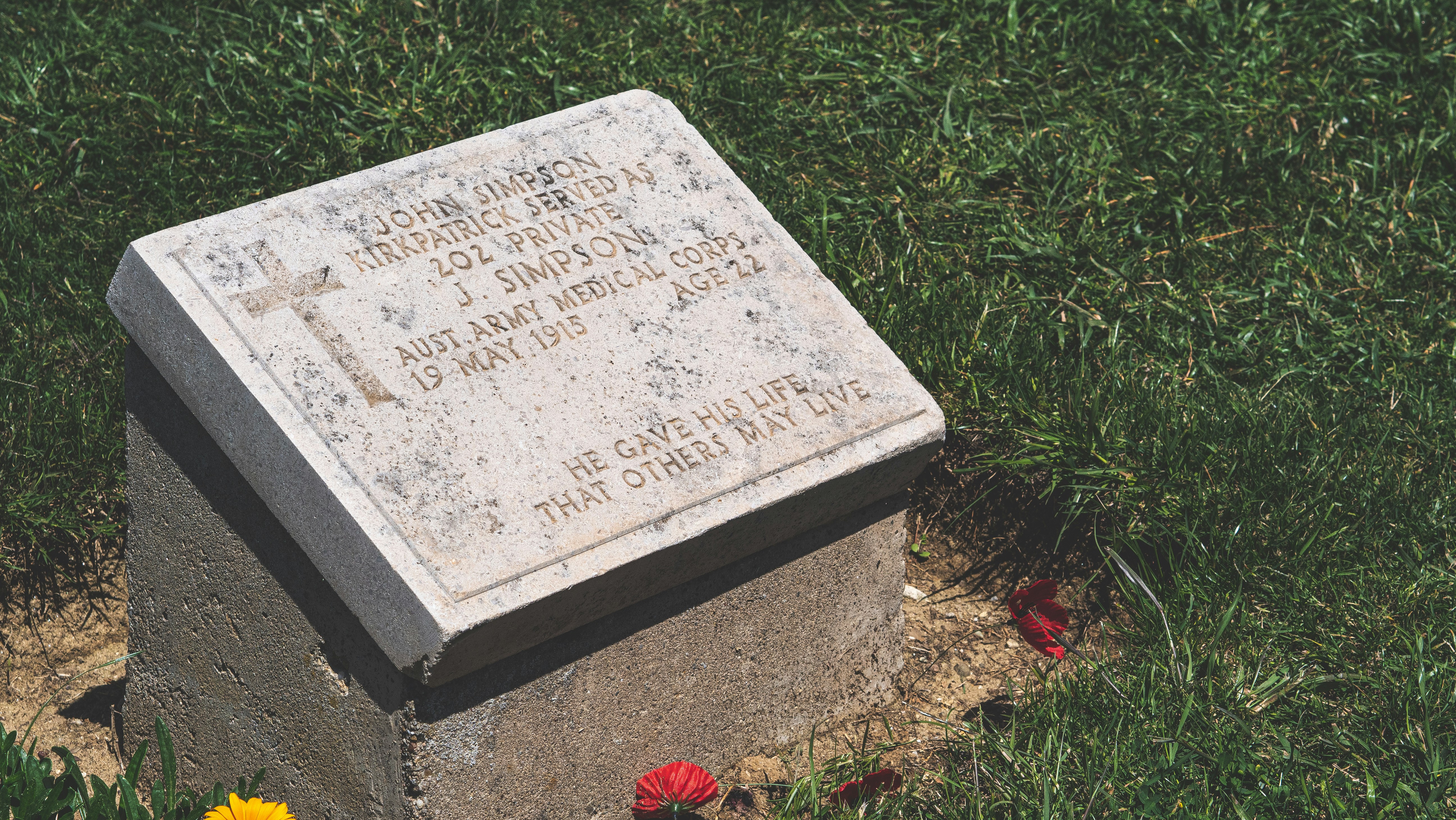 A grave in the grass with flowers around it