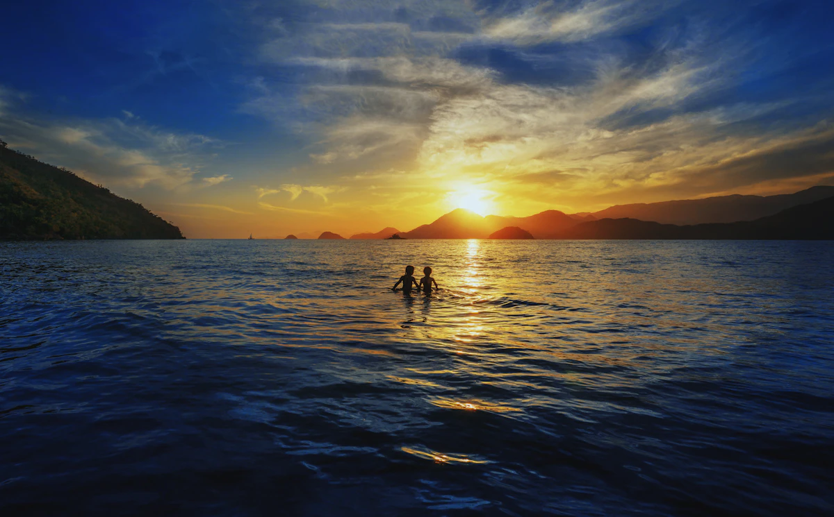 Two people standing on rocks overlooking the ocean at sunset in Ubatuba, São Paulo, Brazil.
