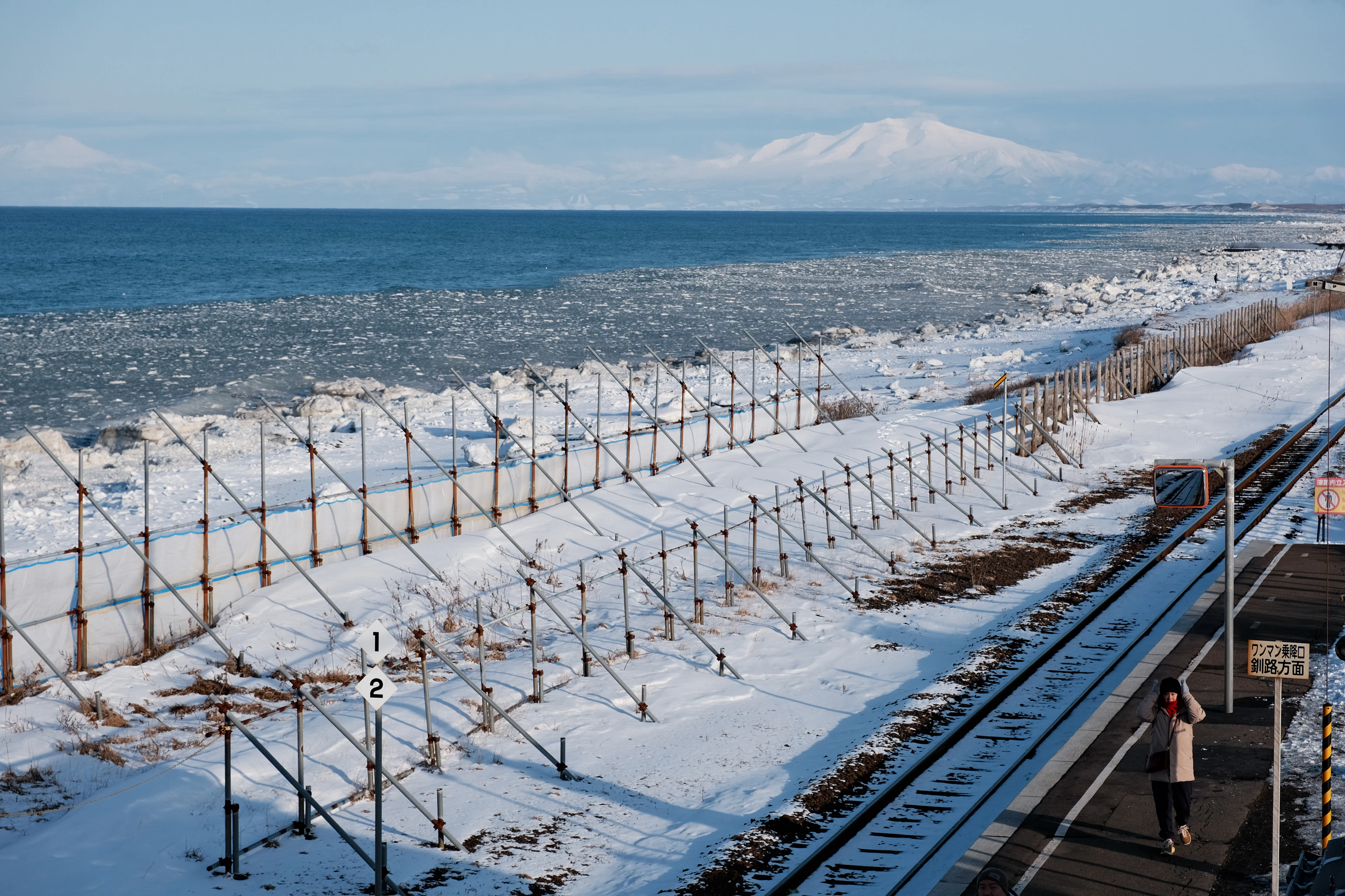 A railway platform on a snow-covered stretch of coast in Hokkaido, with ice in the sea and a snowy peak in the distance