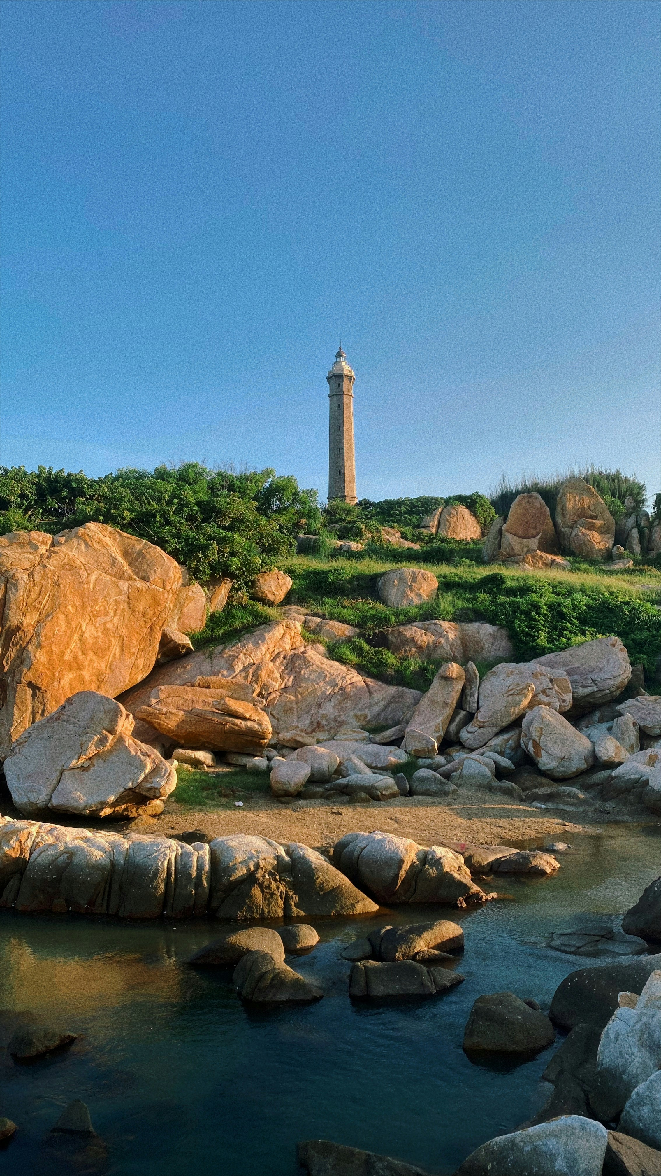 A lighthouse on top of a hill next to a body of water photo – Free ...