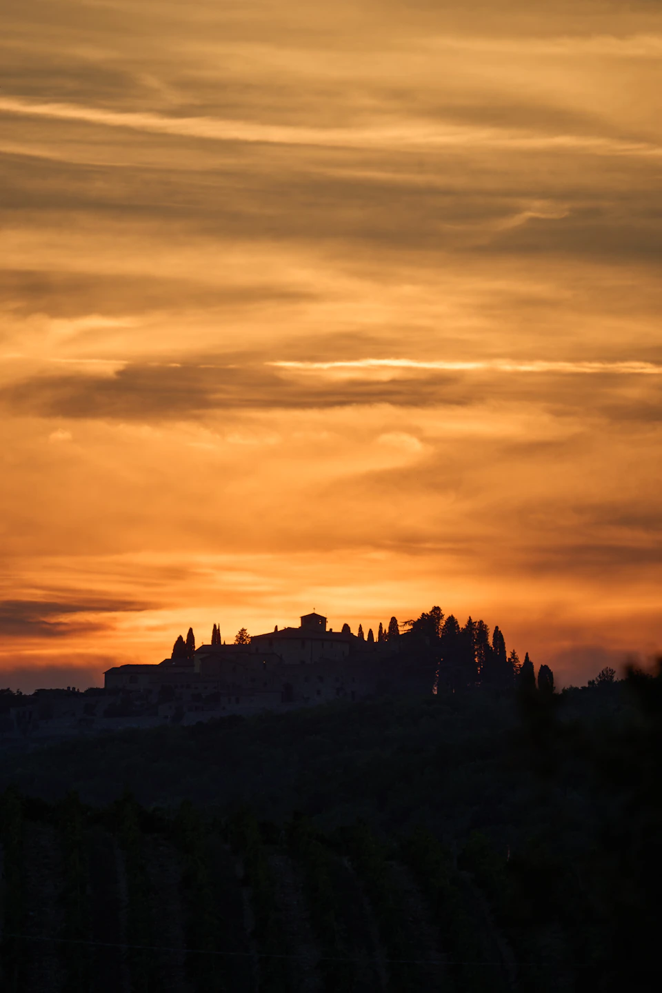Sunset over hillside with large building partially obscured by clouds and silhouettes against vibrant sky