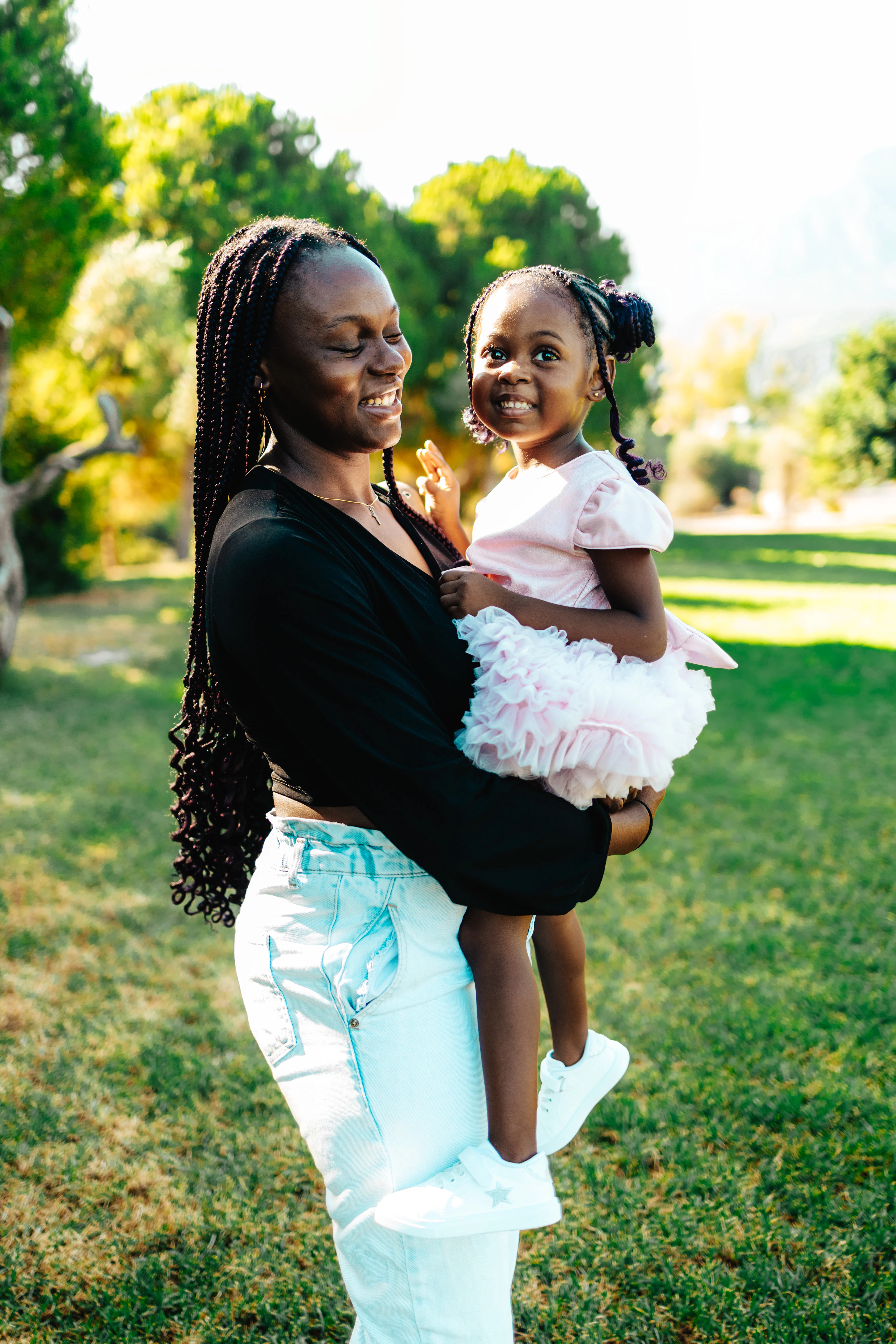 A woman holding a small girl in her arms on a lawn, both smiling