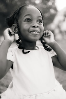 A little girl in a white dress holding a cell phone to her ear