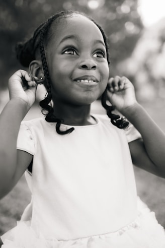 A little girl in a white dress holding a cell phone to her ear