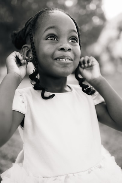 A little girl in a white dress holding a cell phone to her ear