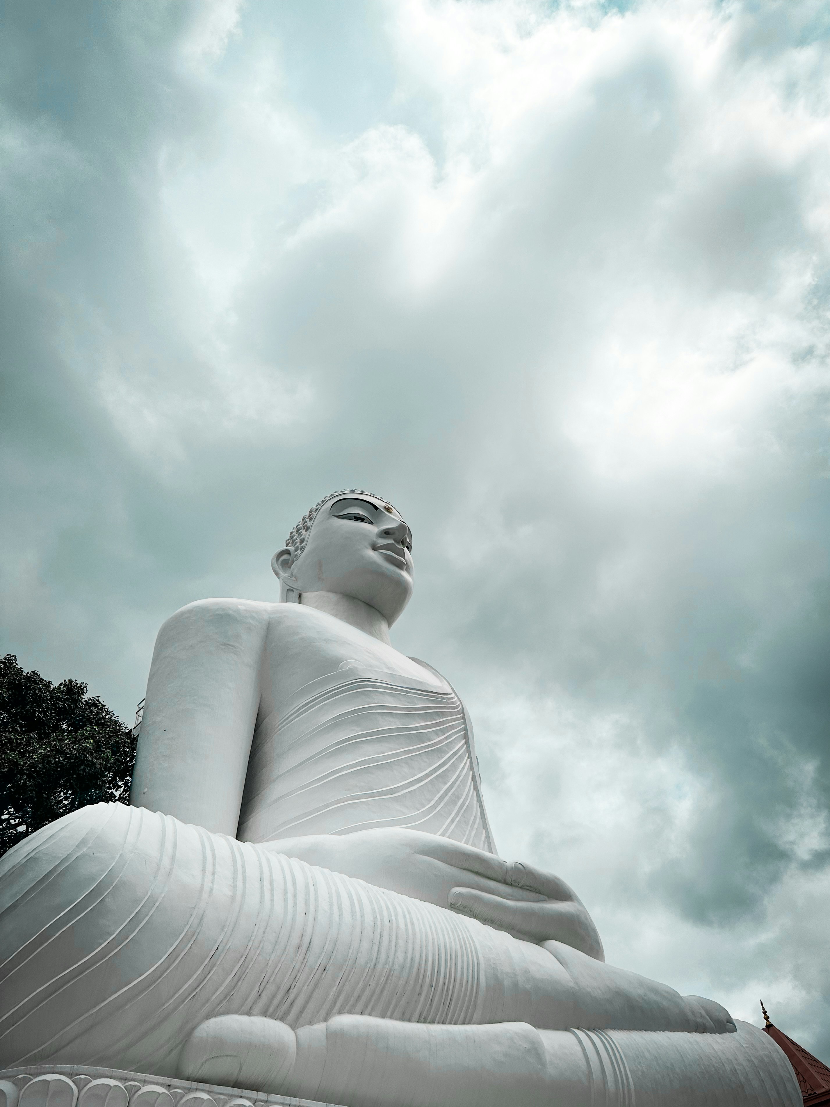 Eine große weiße Buddha-Statue, die unter einem wolkenverhangenen Himmel sitzt