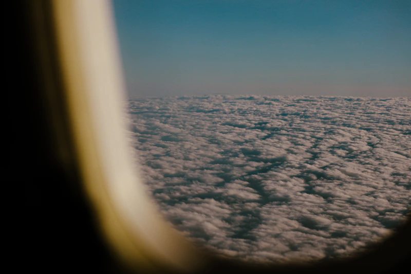 View from airplane window seat showing blue sky and clouds during a long haul flight