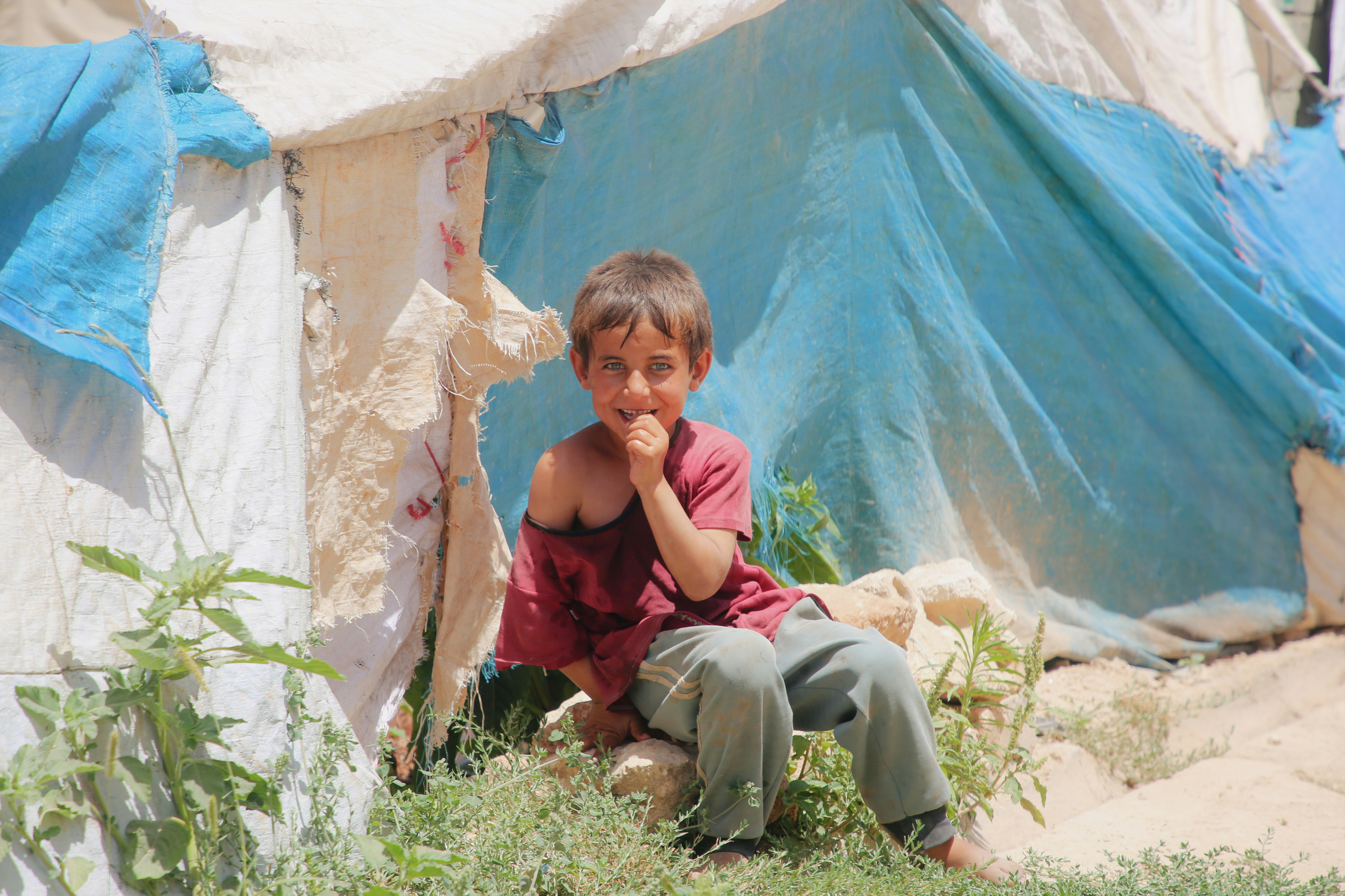 A young boy sitting on the ground in front of a tent