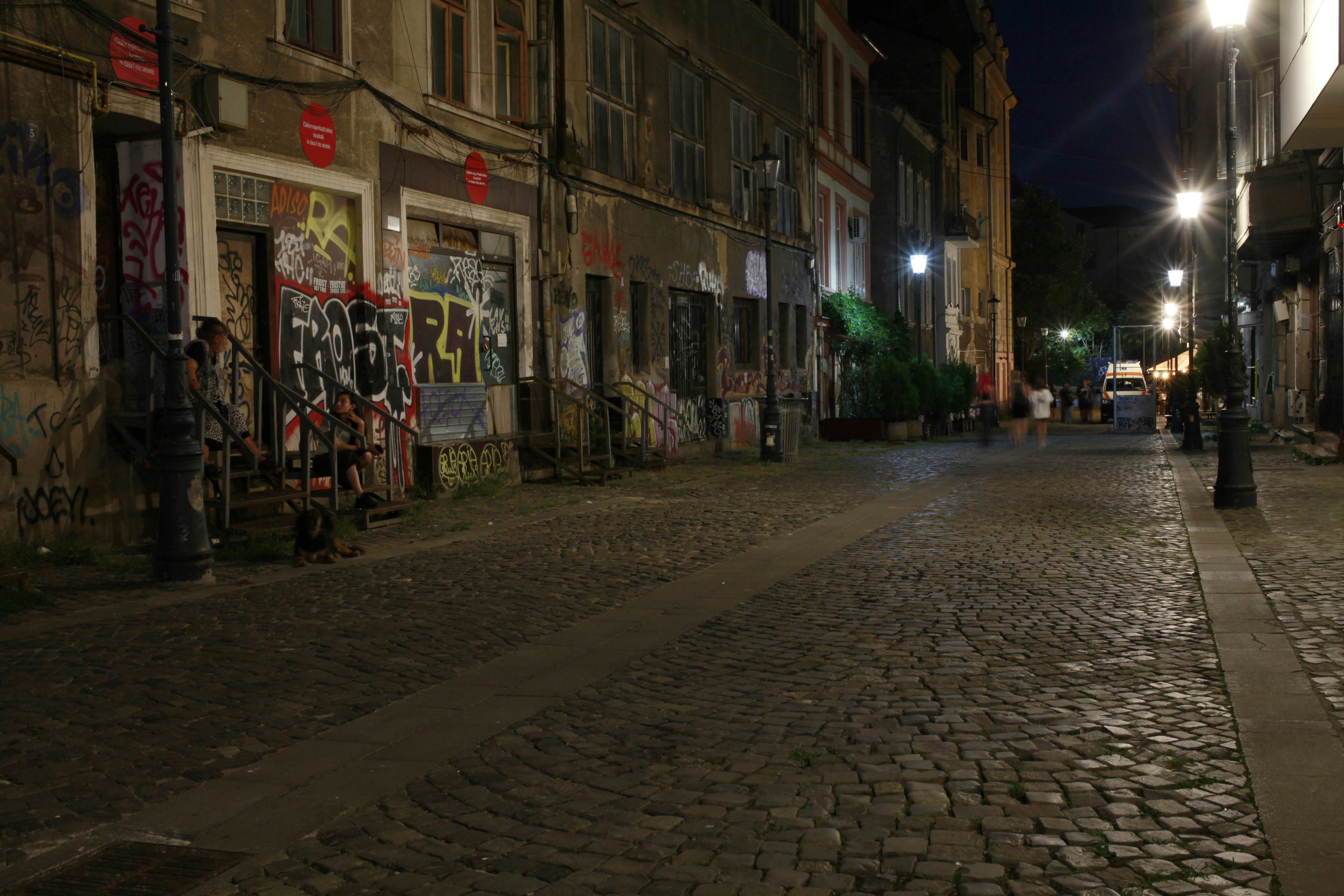 A cobblestone street at night with graffiti on the buildings